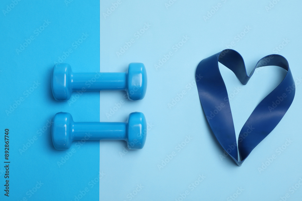 Sticker Two dumbbells and fitness elastic band in shape of heart on light blue background, flat lay. Lovely workout