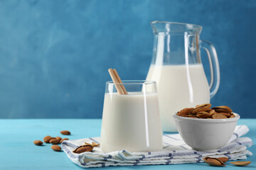 Glass of almond milk, jug and almonds on light blue wooden table, space for text