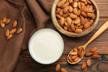 Glass of almond milk and almonds on wooden table, top view