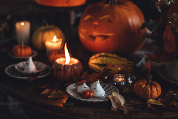 Homemade delicious chocolate cake with coloured orange cream and meringue ghosts, pumpkins for Halloween home party. Elegant beautiful table arrangement with candles, chandelier, Jack-o-Lantern