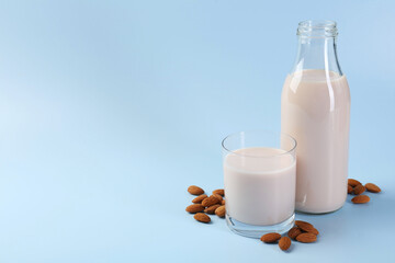 Fresh almond milk in bottle, glass and nuts on light blue background, space for text