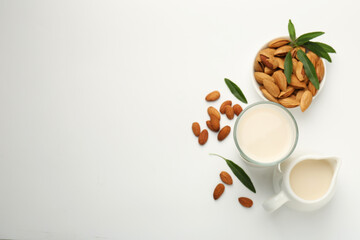 Fresh almond milk in glass, nuts, green leaves and pitcher on white background, flat lay. Space for text