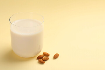 Fresh almond milk in glass and nuts on beige background, space for text