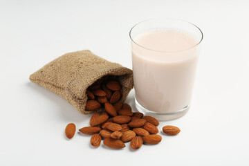 Fresh almond milk in glass, nuts and burlap sack on white background