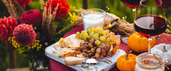 Elegant beautiful dinner table setting for thanksgiving or wedding celebration outdoors, fall countryside style, pumpkin as decor. Romantic atmosphere of a date, sunset. Cheese board, red wine banner