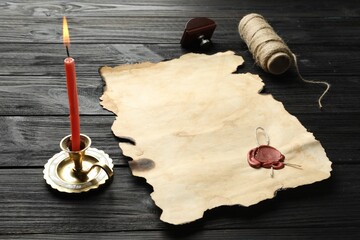Sheet of old parchment paper with wax stamp, twine and candle on black wooden table