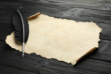 Sheet of old parchment paper and feather on black wooden table