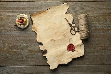 Sheet of old parchment paper with wax stamp, scissors, twine and candle on wooden table, top view