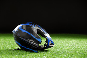 Modern motorcycle helmet with visor on green grass against black background, space for text