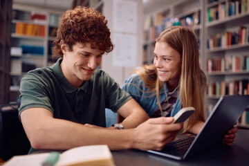 Happy students using wireless technology while learning at university library.