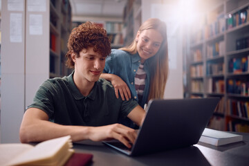 Happy college friends using laptop while studying in library.