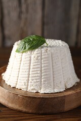 Fresh ricotta (cream cheese) with basil on wooden table, closeup