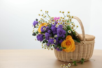 Wicker basket with beautiful flowers on light wooden table, space for text