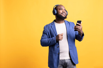 Relaxed african american man having fun listening to music from mobile phone. Carefree BIPOC person hearing tunes playing from smartphone device, isolated over studio background