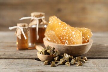 Natural honey tincture, propolis granules and sweet honeycombs on wooden table, closeup