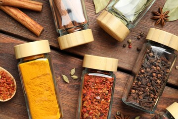 Different spices in glass jars on wooden table, flat lay