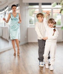 Boy with pair girl in sport wear train to dance vigorous hustle during classes. Children rehearse contemporary dancing movement. Female teacher conducts class for students