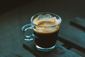Cup of black espresso coffee with brown foam on a wooden table on cafe terrace. Hot drink outdoors on dark blue grey background. Autumnal beverage.