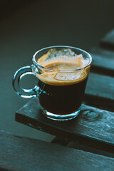 Cup of black espresso coffee with brown foam on a wooden table on cafe terrace. Hot drink outdoors on dark blue grey background. Autumnal beverage.