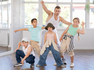 Fototapeta premium Cheerful preteen children, boys and girls, striking dynamic dance poses with young male instructor in bright sunlit studio, showcasing creativity and teamwork during hip-hop dance class