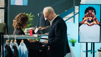 Woman retail clerk showing multiple tie colors to customer, helping him to match formal suit with...