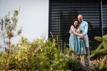 Portrait of happy family spending time together outdoors. Mother and father holding daughter, standing on terrace.