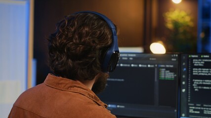 Man doing IT support job from apartment office, drinking cup of coffee and listening music while coding. Developer with headphones on enjoying hot tea and writing code on computer, camera A close up