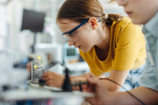 Two classmates working together on circuit board, building robot in after-school robotics club. Children learning robotics in Elementary school.