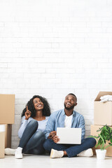 Young african couple sitting on floor at new home and looking at copy space, using laptop