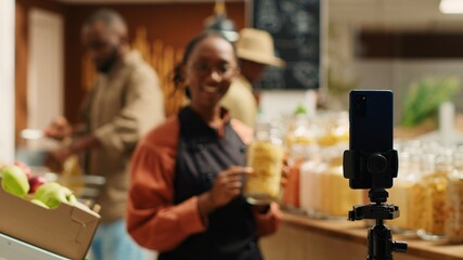 African american vendor presenting variety of pasta in jars, discussing about ethically sourced products and homemade food alternatives. Filming promotional video for healthy lifestyle. Camera 1.