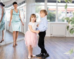 Boy paired up with girl during ballroom dancing lesson. Children rehearse waltz while female...