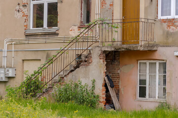Stary, lekko podniszczony dom z cegły w centrum miasta. Wysokie schody ze stalową poręczą prowadzące do wejścia do domu  (zabytkowy i zniszczony). © Grzegorz