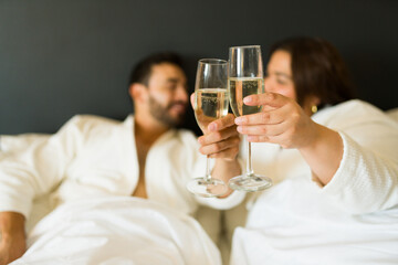 Joyful pair in bathrobes raising glasses of champagne during a romantic escape in a hotel suite