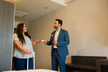 Fototapeta premium Hotel manager presents room key card to female guest with luggage, smiling warmly