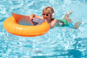 Child swimming on an inflatable ring with a laptop water pool. Little freelancer using computer, remote working in swimming pool.