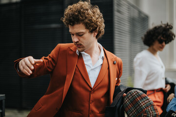 Young professional man in a stylish orange suit adjusting his jacket while standing outdoors. Confident and fashionable business attire.
