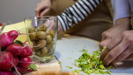 Two people preparing a fresh healthy salad with olives and radishes.