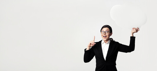 Business Idea. Excited Businesswoman Holding Empty Speech Bubble Pointing Finger Up Over White Studio Background. Mockup