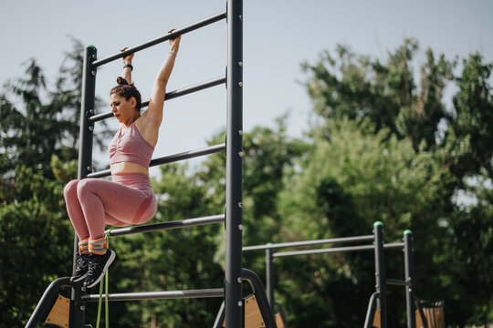 Athletic woman performing calisthenics exercises on monkey bars in an outdoor park. Focus on strength and fitness. - Powered by Adobe