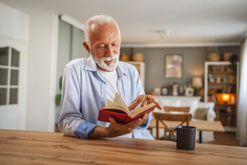 Senior caucasian man read a book and drink cup of coffee at home