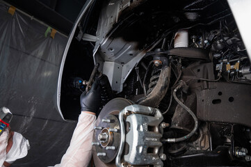 An auto mechanic applies anti-corrosion mastic to the underbody of a car.