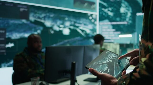 Military officer leads cybersecurity operations in a high tech operation room command post, ensuring data protection. Soldiers working with cctv surveillance systems, satellite imagery. Camera B.