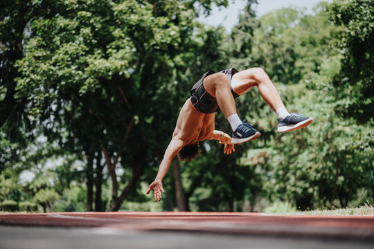 Athletic man performing a dynamic back-flip outdoors in a park setting, showcasing athleticism, fitness, and agility.