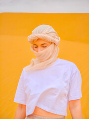 Portrait of a young woman with a scarf in Sahara desert. Girl with a traditional Arabic hijab standing on a golden sand