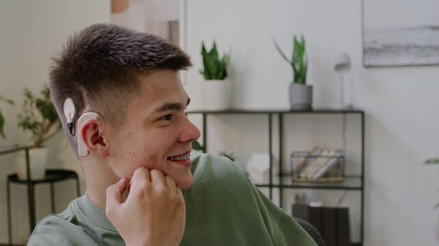 Close-up shot of young Caucasian man with hearing impairment, wearing cochlear implant and tooth braces, having conversation using American sign language, smiling and laughing