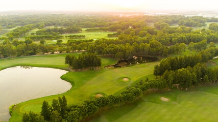 Obraz premium Golf course at sunset with beautiful sky and sand trap. Scenic panoramic view of golf fairway with bunker. Golf field with pines