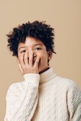 A young african american boy in a white sweater covering his mouth with his hand, expressing surprise or shock