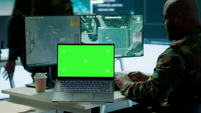 IT expert collecting real time information next to isolated chroma key screen, high tech gear in command post. Soldier processing intelligence for field operations and strategic missions. Camera A.