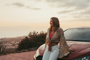 One young beautiful woman sitting on car outdoor looking at the sunset having fun. Blonde millennial girl feeling good and free at evening..