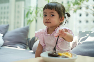 Young girl in a pink dress enjoying a chocolate dessert at a cozy cafe with a sunny and tranquil atmosphere.